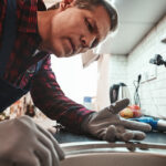 Inside view. Close-up of handsome plumber repairing sink in kitchen